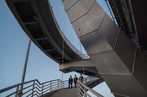Free Two businessmen in suits under modern metal architecture with a blue sky. Stock Photo