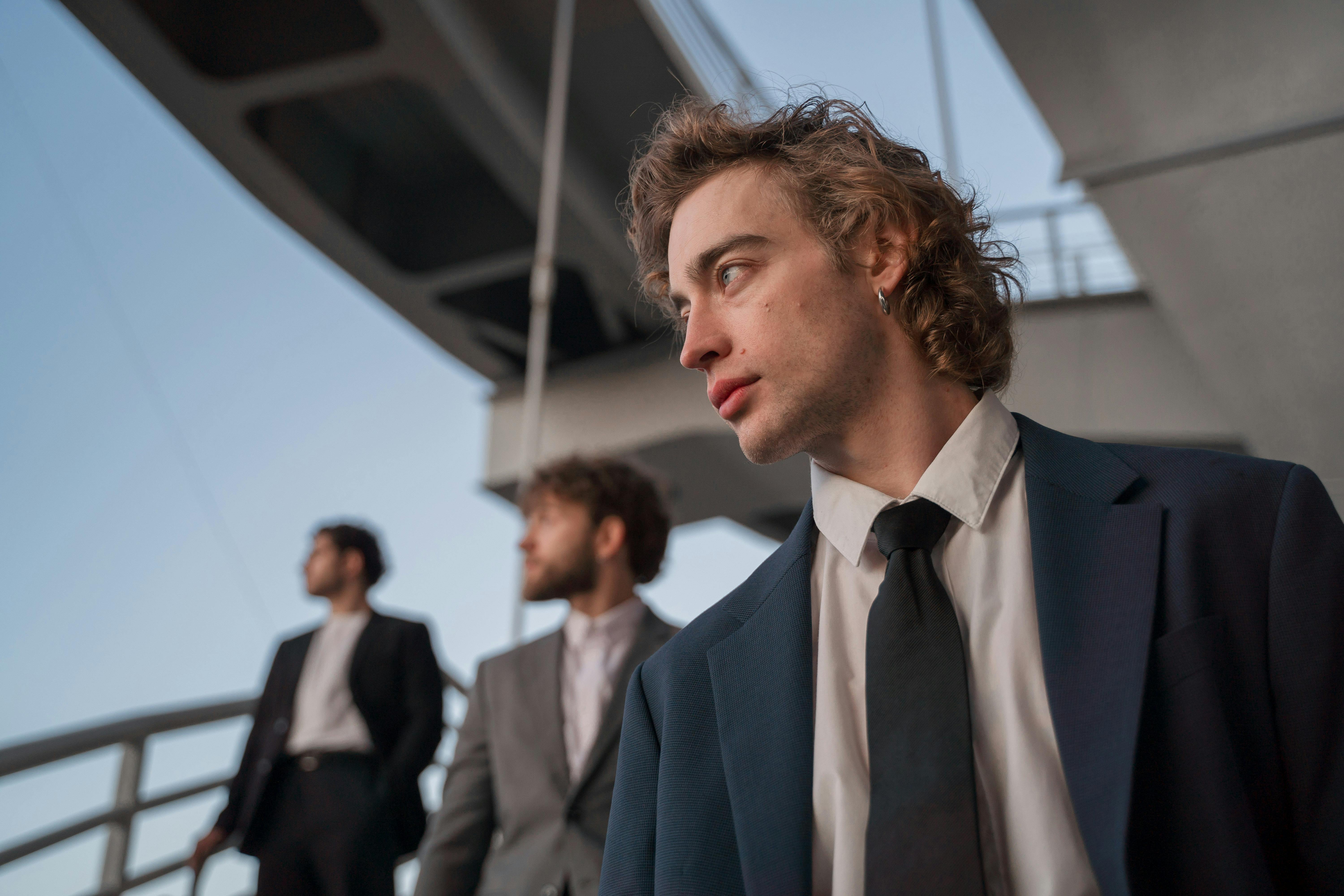 Stylish young men in suits posing outdoors with modern architecture backdrop.