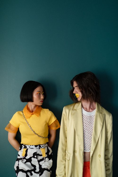Free Trendy couple in vibrant outfits posing against a teal backdrop. Fashion-focused image. Stock Photo