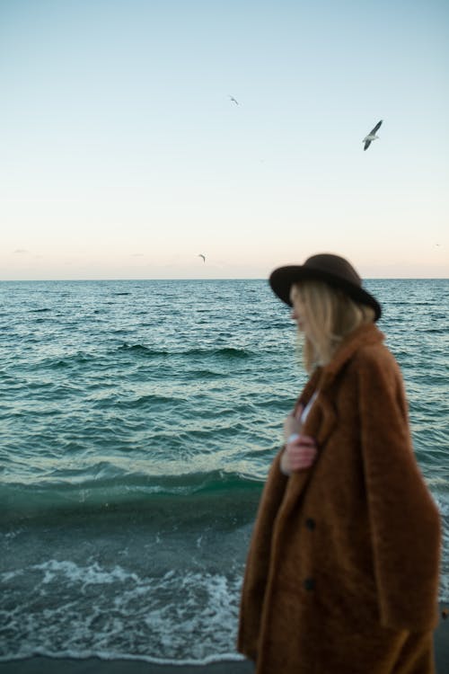 Woman in Brown Coat Standing Beside Sea Water