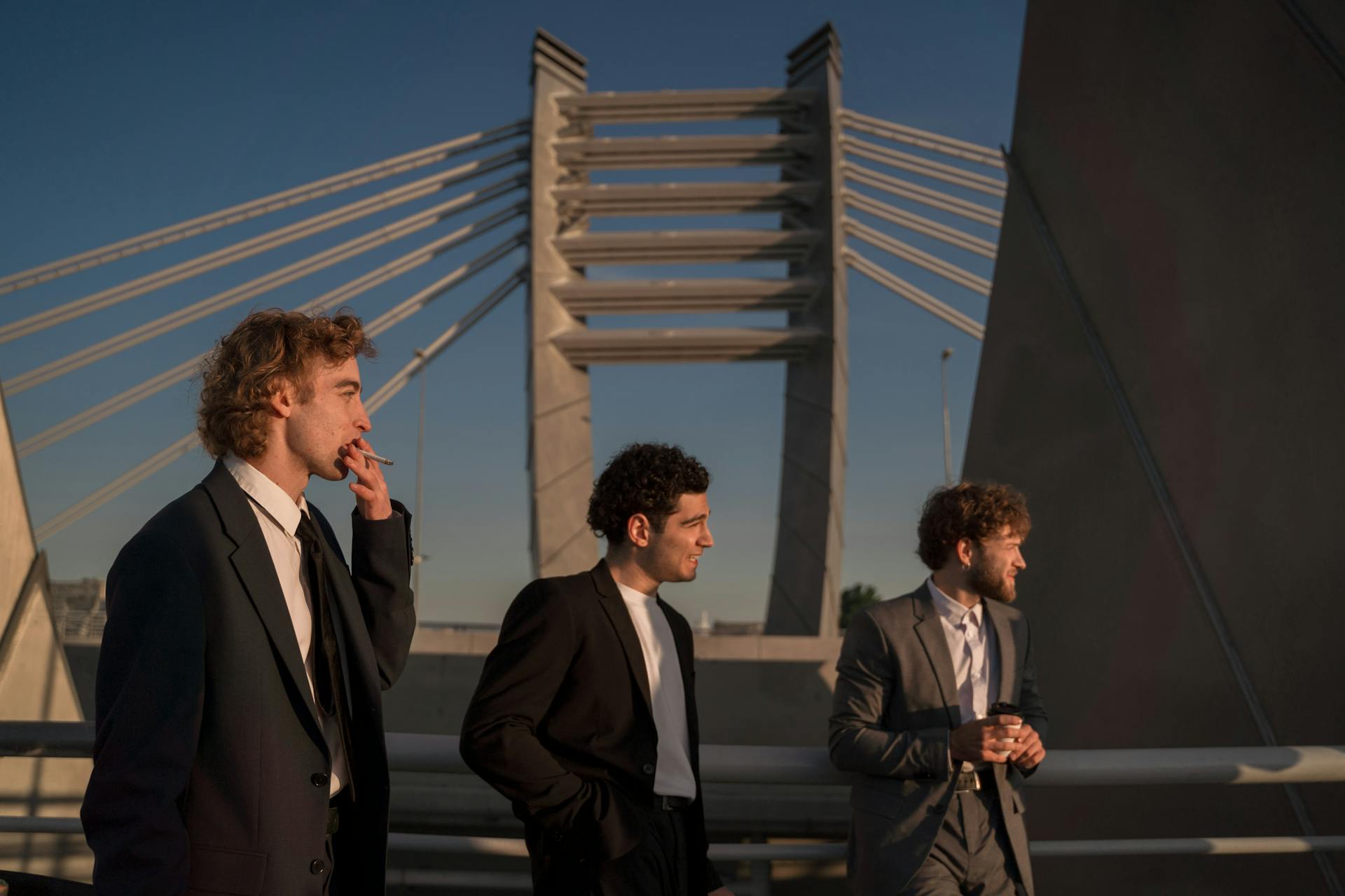 Three businessmen in suits standing on a bridge at sunset, exuding confidence and style.