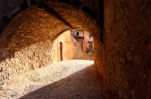 Free Sunlit cobblestone alleyway under an ancient tunnel in Santo Stefano di Sessanio, Italy. Stock Photo