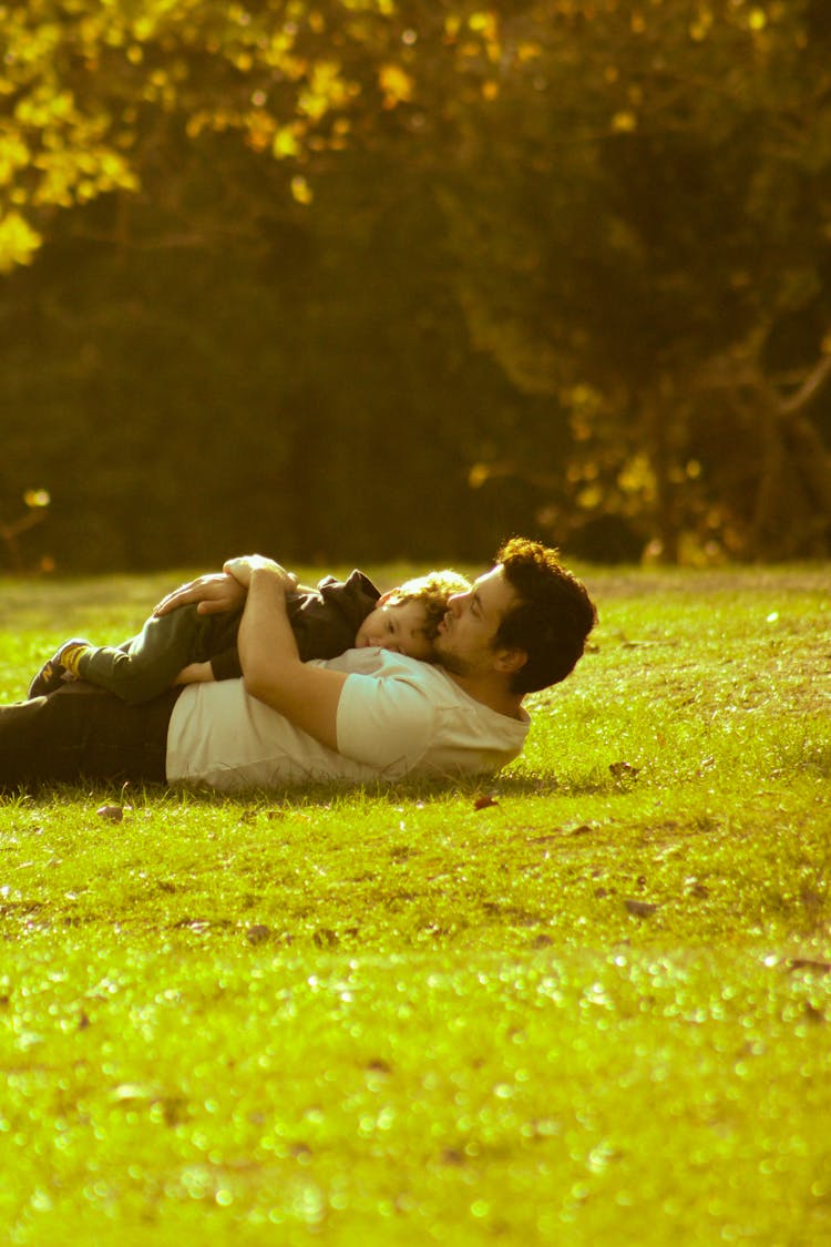 Man And His Child Lying On Green Grass