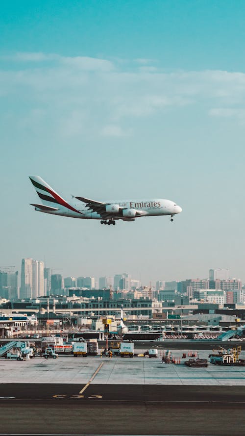 White and Red Passenger Plane Flying over City Buildings