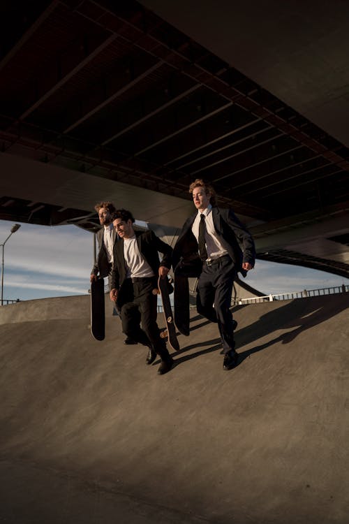 Men in Black Suit Holding Skateboards while Running on a Ramp