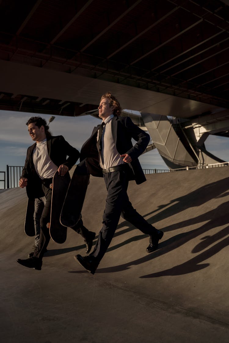 Two Men Holding Skateboards Running On Skate Ramp