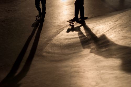 Free Captivating silhouettes of skateboarders casting long shadows in a skate park at dusk. Stock Photo