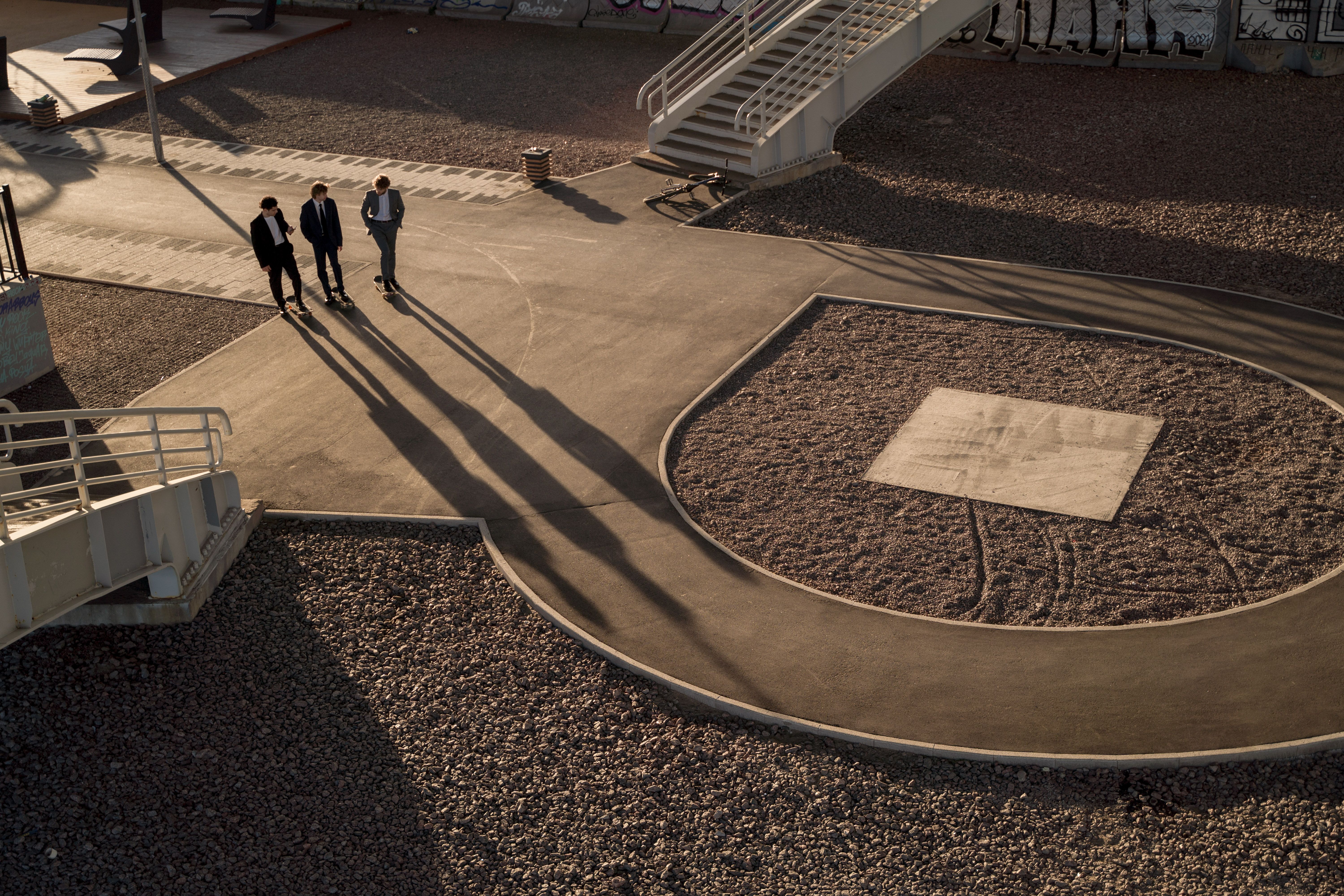 Three businessmen walk on a modern urban pathway casting long shadows at sunset.