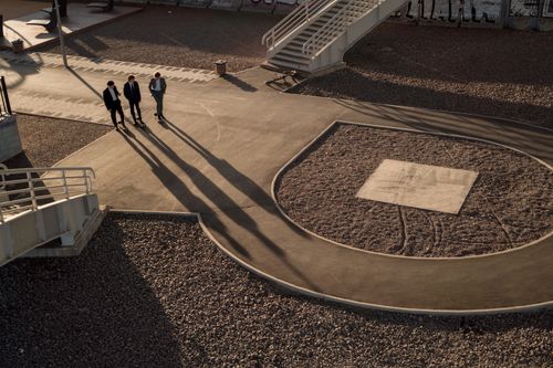 Free Three businessmen walk on a modern urban pathway casting long shadows at sunset. Stock Photo