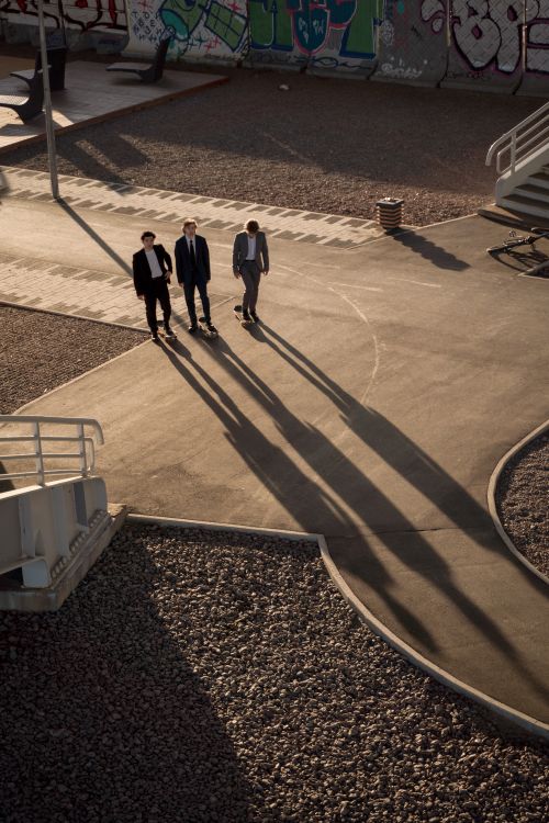 Free Aerial view of three men in suits skateboarding in a sunlit, urban skatepark with prominent shadows. Stock Photo