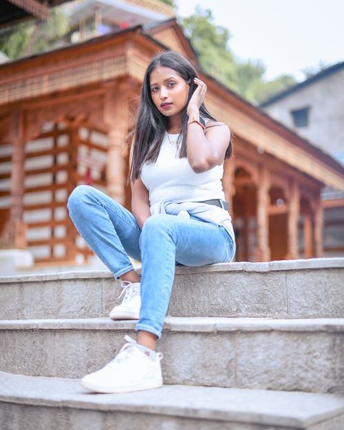 Free Fashionable young woman sitting on concrete stairs in casual jeans and white top. Stock Photo