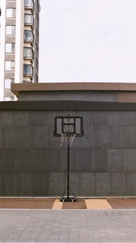Vertical shot of a basketball hoop against a concrete wall in an urban setting with a building in the background.