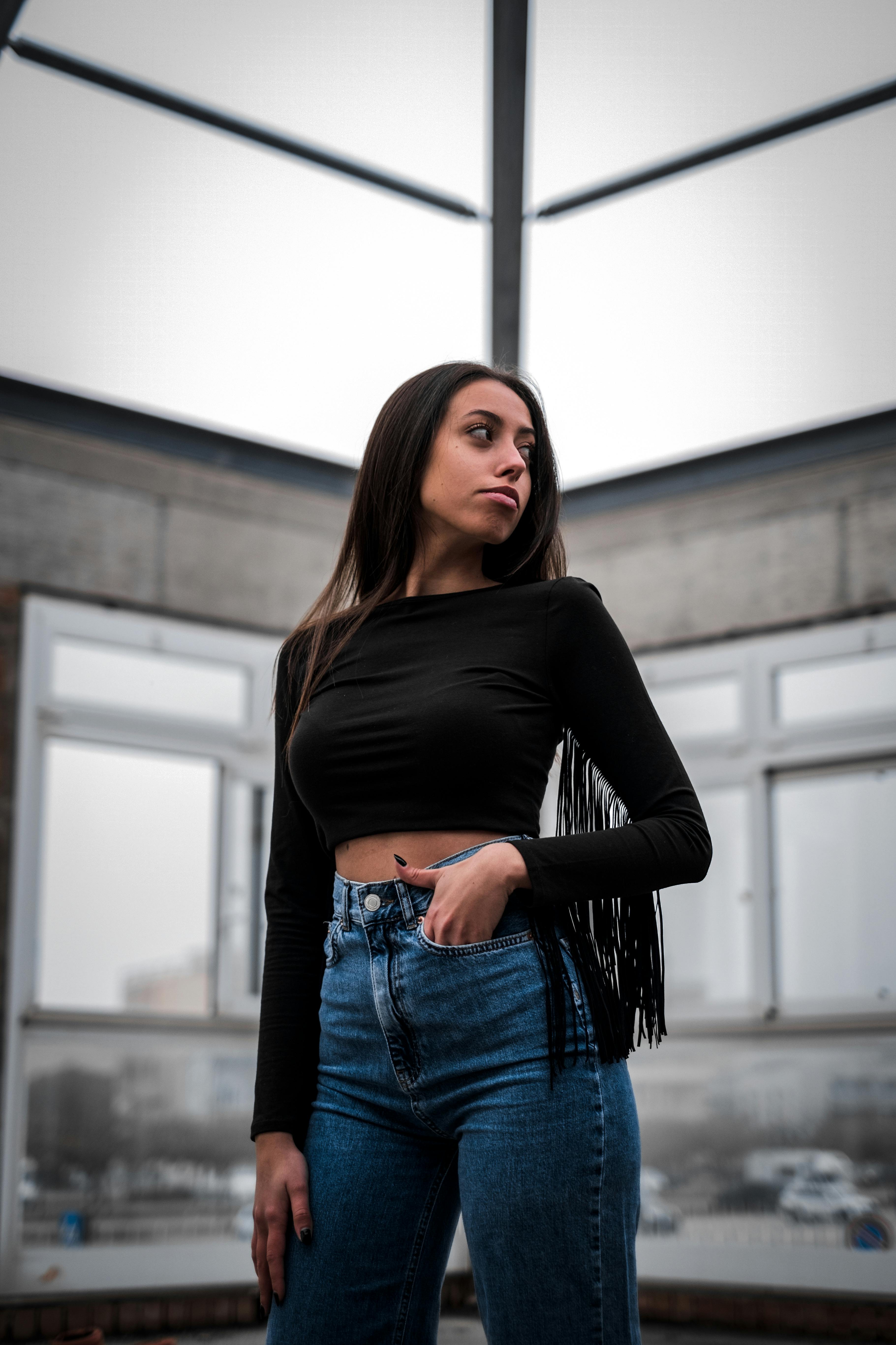 A Sexy Woman in Black Long Sleeves Crop Top and Denim Jeans Standing while  Looking Afar · Free Stock Photo
