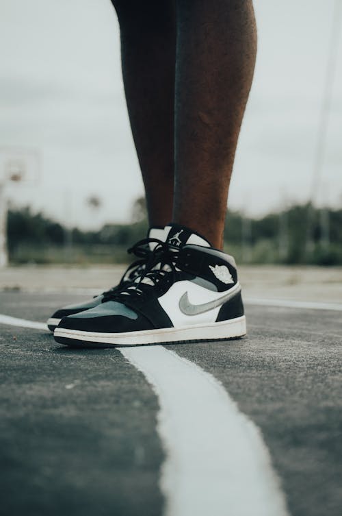 A Person Wearing Nike Sneakers while Standing on an Asphalt Ground