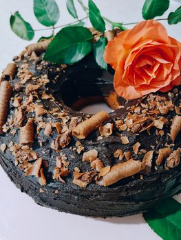 Close-up of a chocolate cake adorned with an orange rose and green leaves, highlighting its intricate toppings.