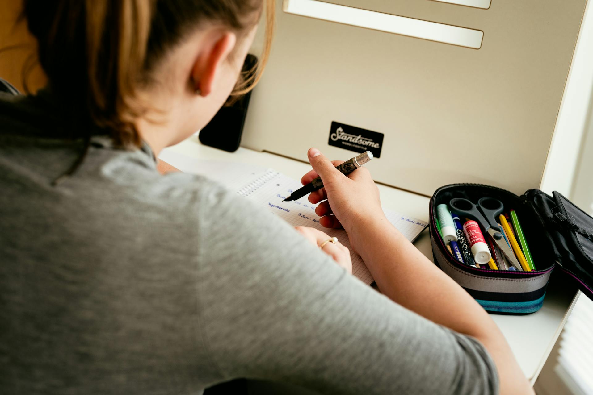 A person writing in a notebook at a desk with stationery, focusing on study or work.