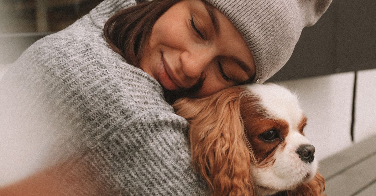 A woman hugging her beloved Cavalier King Charles Spaniel outdoors in authentic natural light.