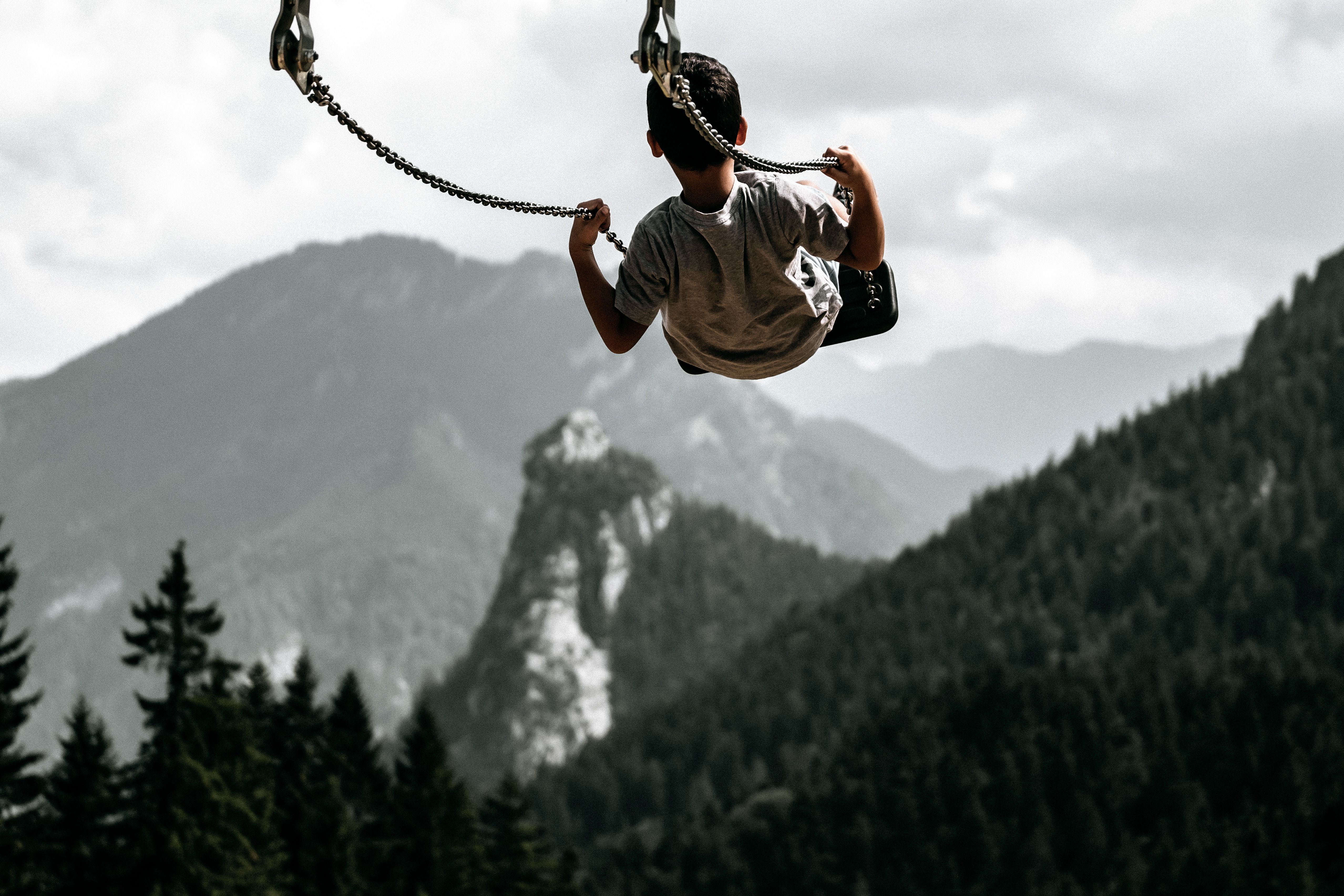 A young boy swings high above picturesque mountains, embracing adventure and freedom.
