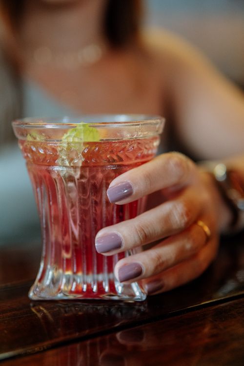 Free Close-up of a hand holding a red cocktail glass with an ice and lime garnish. Stock Photo