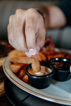 Close-up of hand dipping a crispy fry into delicious creamy sauce indoors.