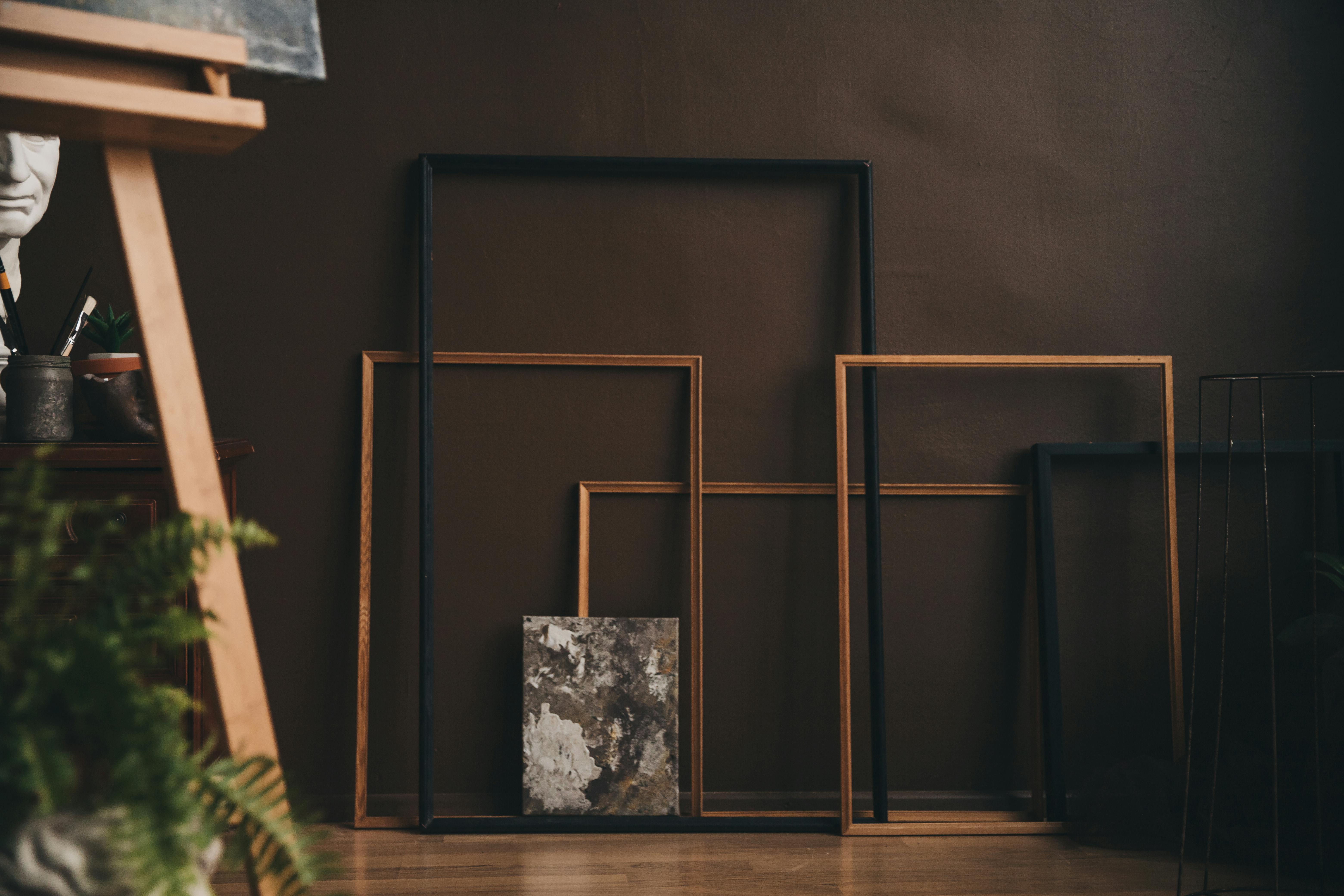 Aesthetic arrangement of wooden picture frames in a dimly-lit art studio with an easel.