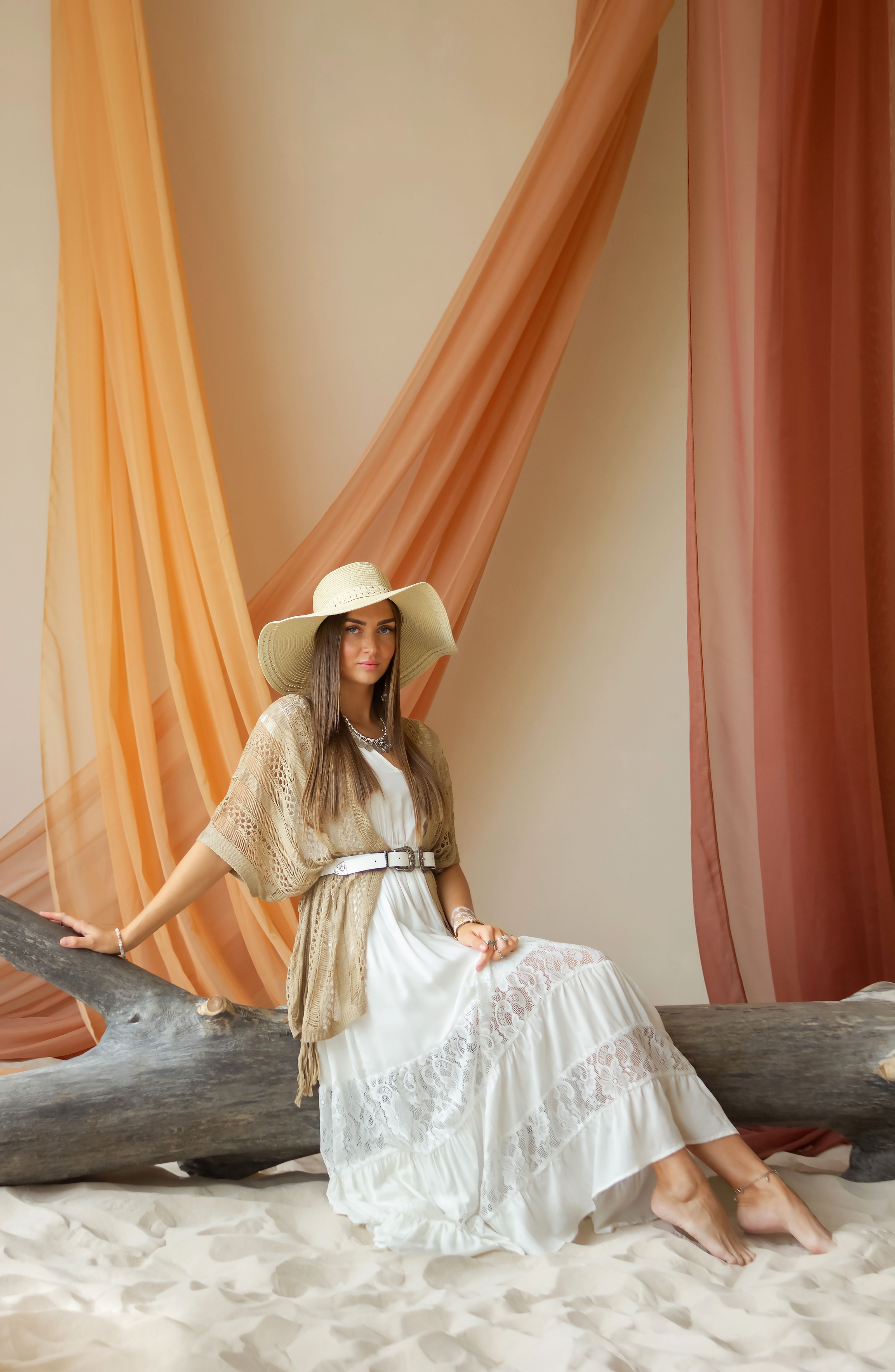 Uma mulher estilosa posando elegantemente em um ambiente interno com um vestido branco e chapéu, exibindo calor e graça.