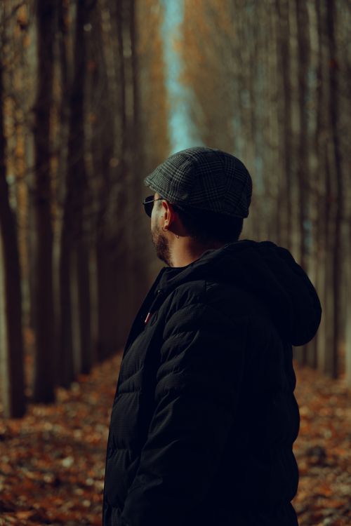 Free A man in a black jacket and flat cap stands in an autumn forest. Stock Photo