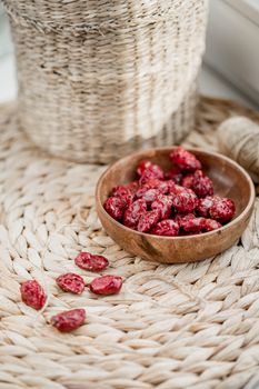 Dried red berries elegantly displayed in a wooden bowl on a woven placemat.
