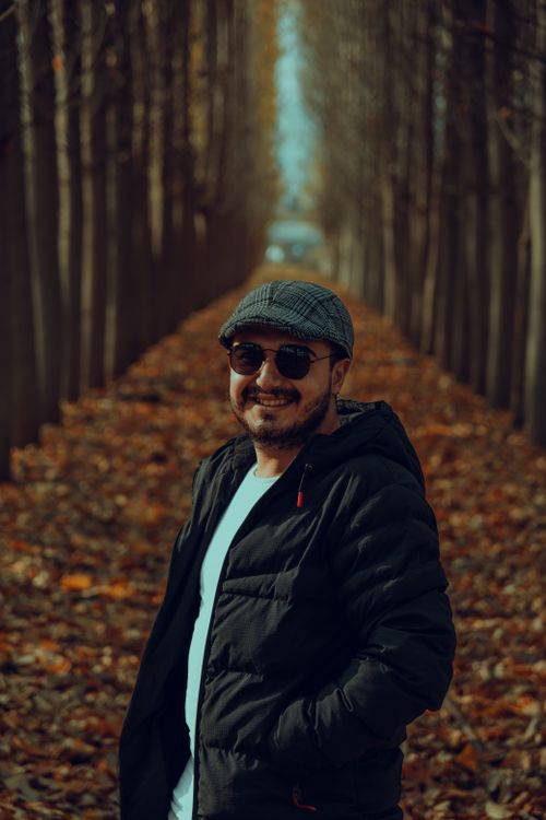 Free Man wearing a black jacket and sunglasses smiles on a leaf-covered forest path in fall. Stock Photo