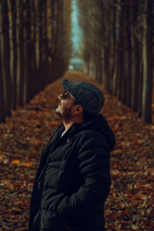 Free Man in a black jacket and hat standing in an autumn forest, looking upwards. Stock Photo