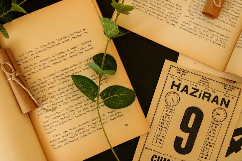 Artistic arrangement of an open book, leaves, and a vintage calendar shows a nostalgic scene.