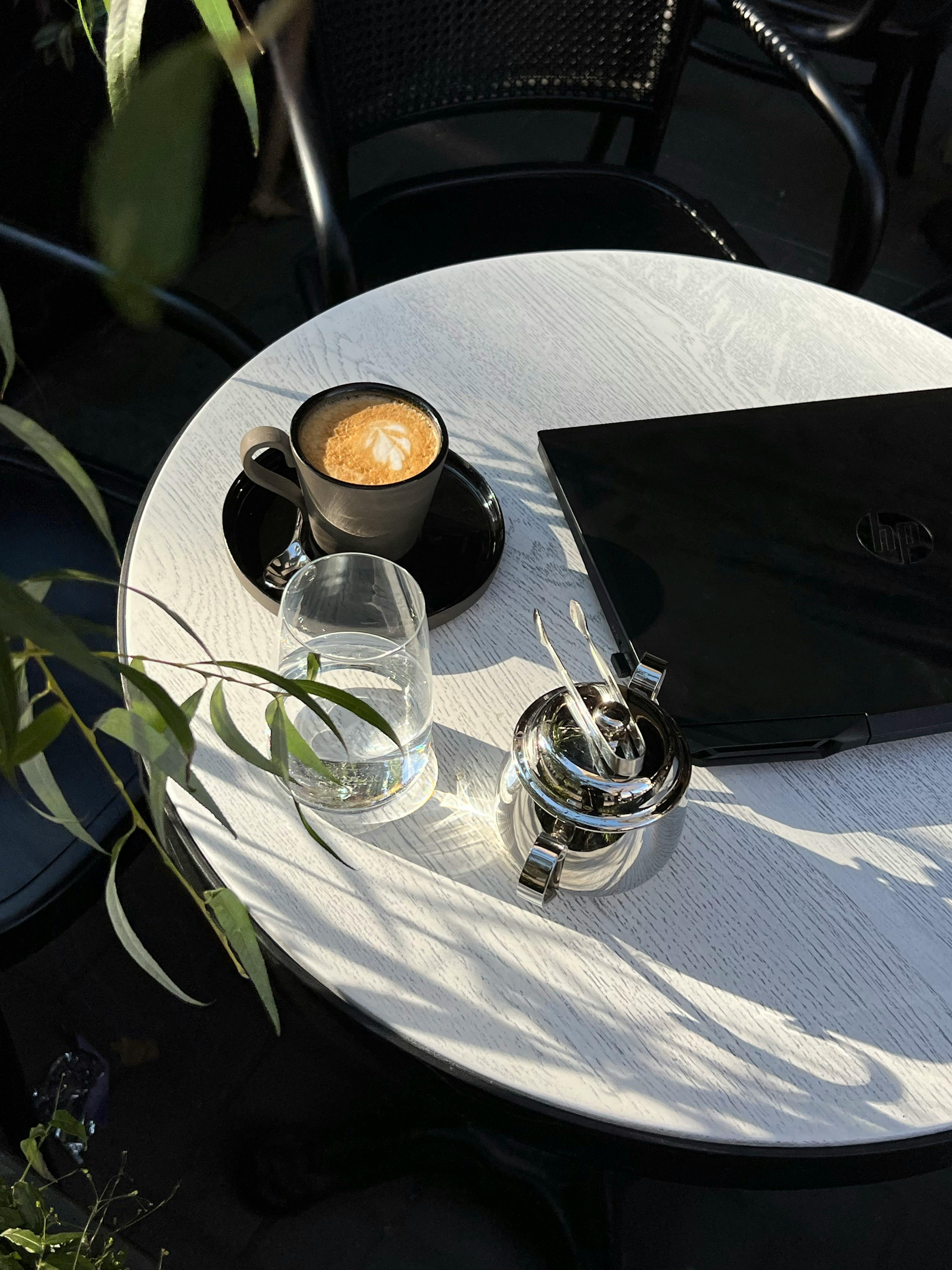 A serene café table setup featuring coffee, laptop, and sunlight in Odesa, Ukraine.