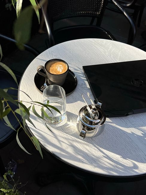 A serene café table setup featuring coffee, laptop, and sunlight in Odesa, Ukraine.