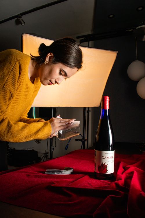 Free A woman arranges a photoshoot setup with wine bottle and lighting in a studio. Stock Photo