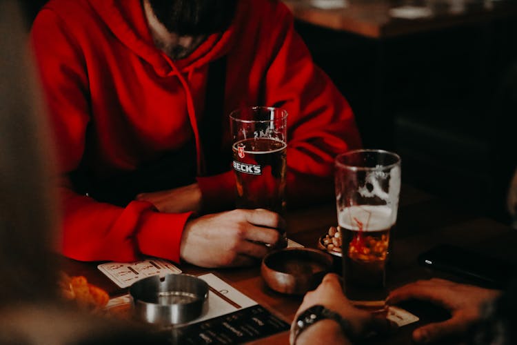 People Holding The Glasses Of Beer On The Table