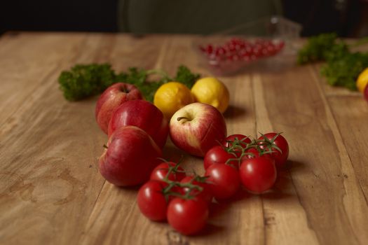 Colorful mix of apples, lemons, cherry tomatoes, and parsley on a rustic wooden table.