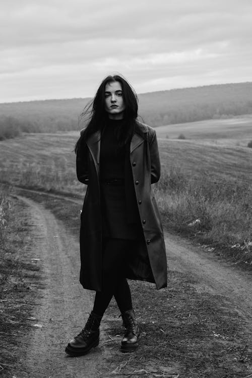 Woman in Black Coat Standing on Field in Grayscale Photography