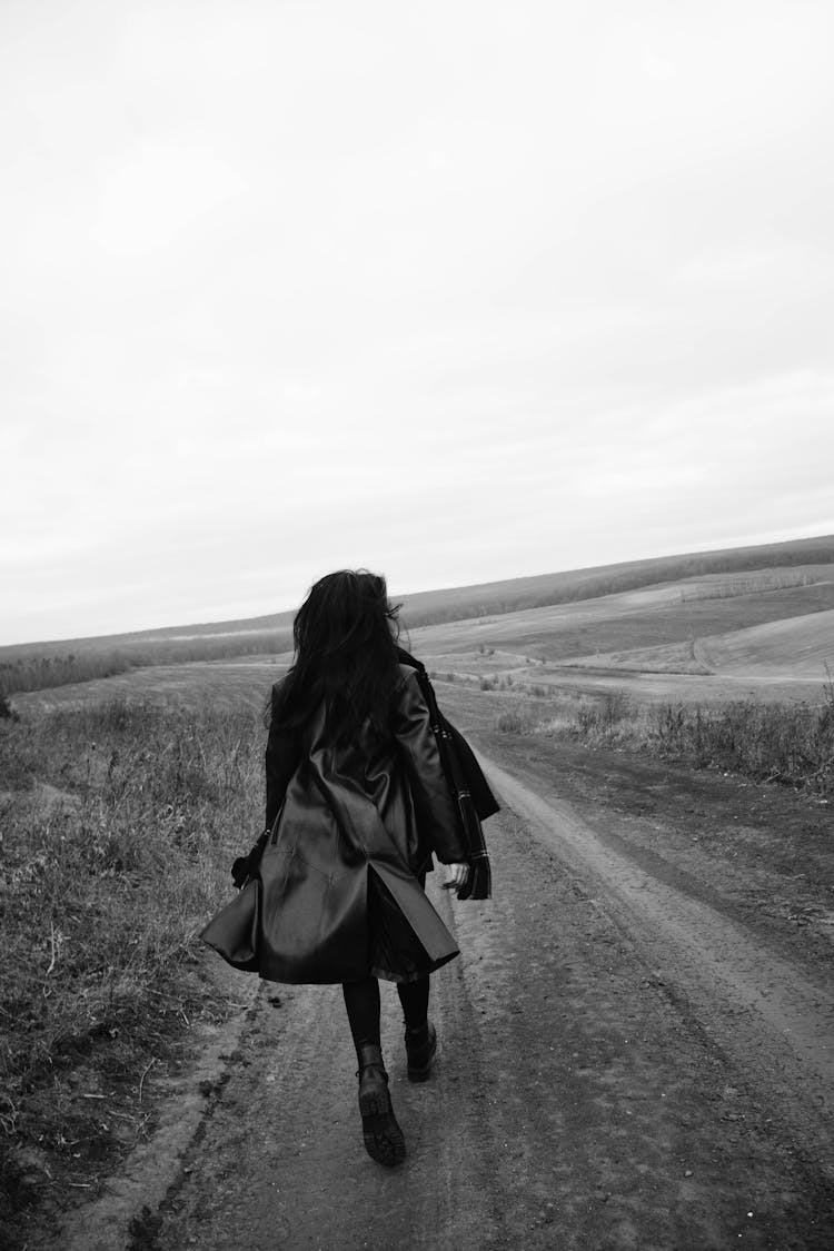 Woman In Leather Jacket Walking Road In Field