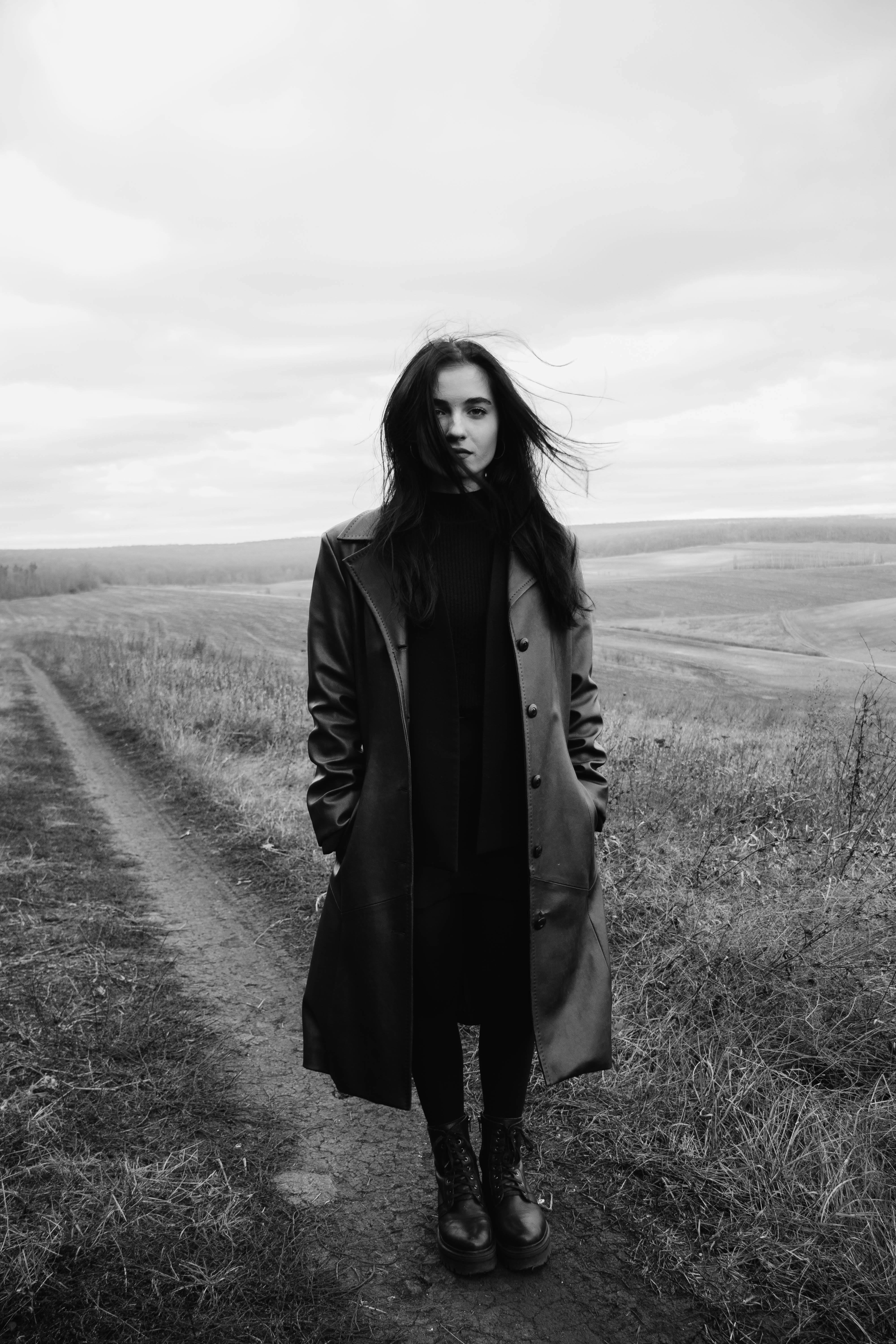 Elegant portrait of a woman in a coat standing in a serene open field.