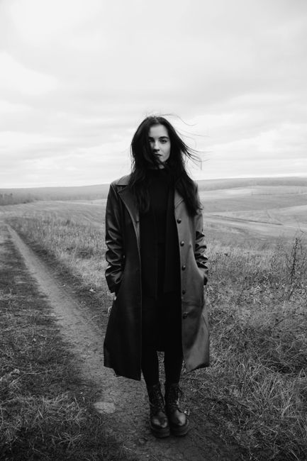 Elegant portrait of a woman in a coat standing in a serene open field.