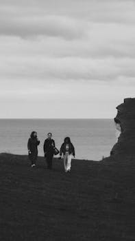 Group of people walking near dramatic cliffs, captured in monochrome in England's countryside.
