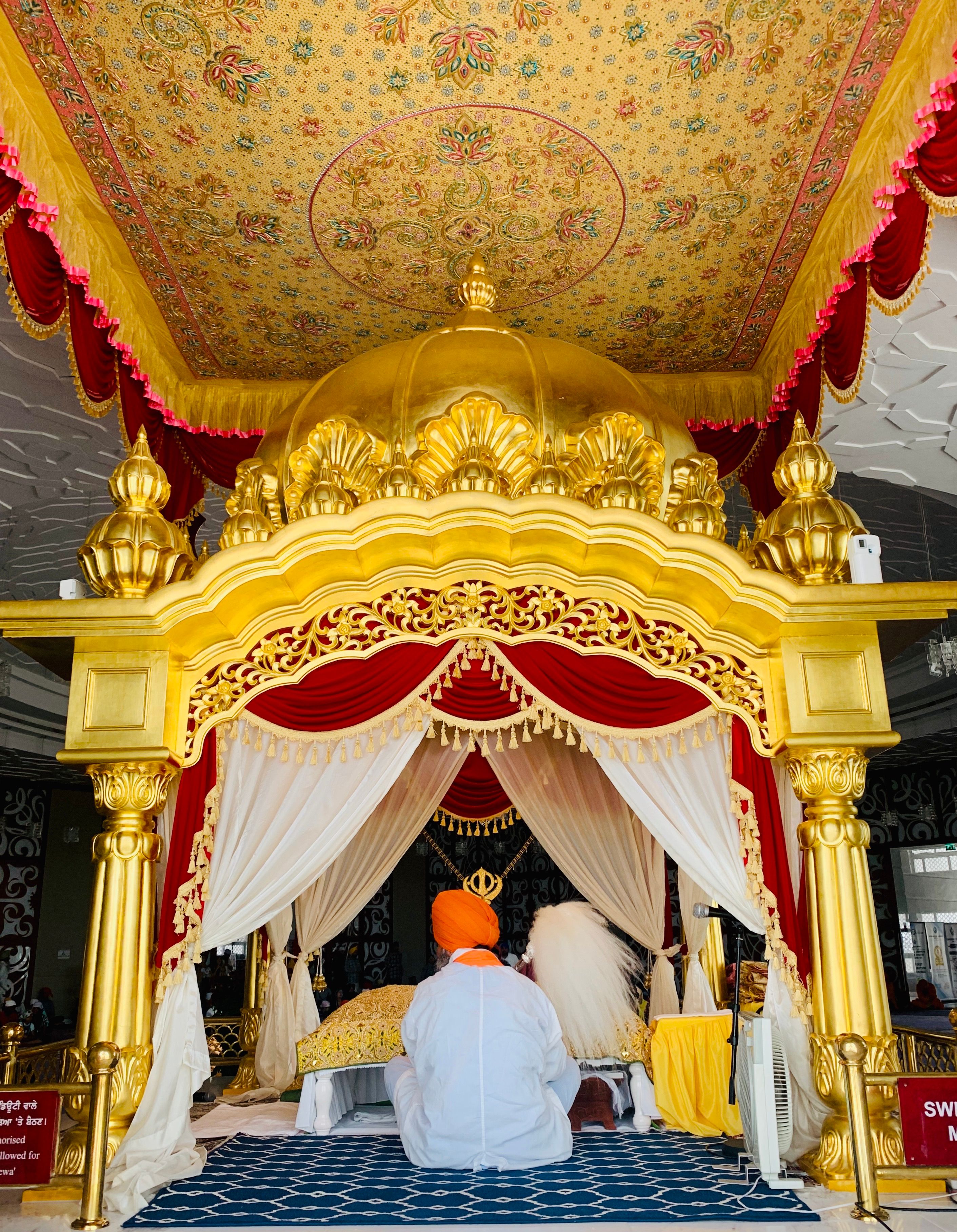 A man in traditional attire sits before an ornate golden temple canopy in peaceful meditation.