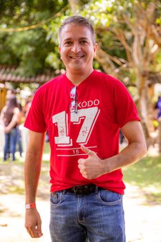 A cheerful man in a red shirt with '17' printed, giving a thumbs up outdoors.