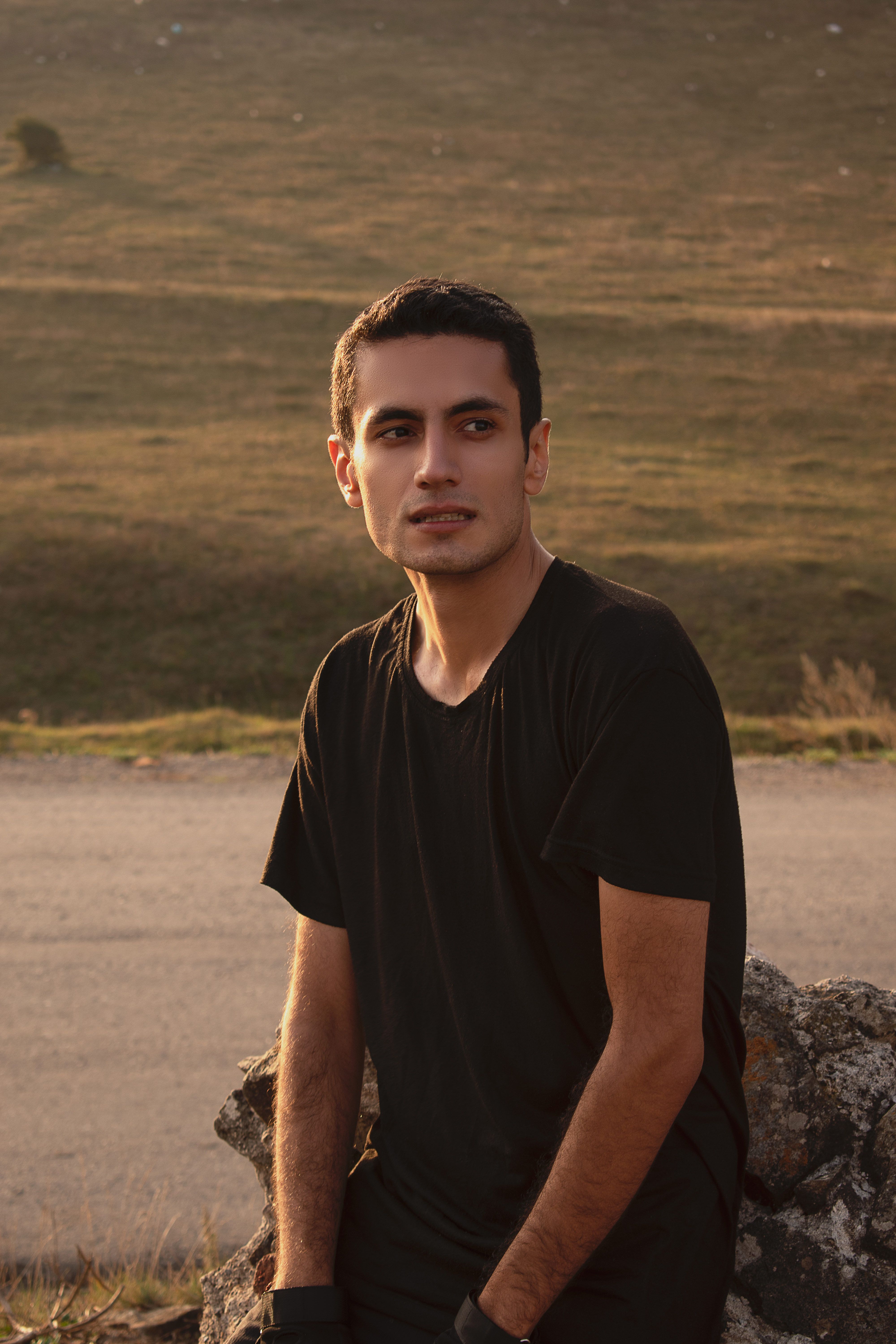 A young man in casual attire sits on a rock, warmly lit by the setting sun.