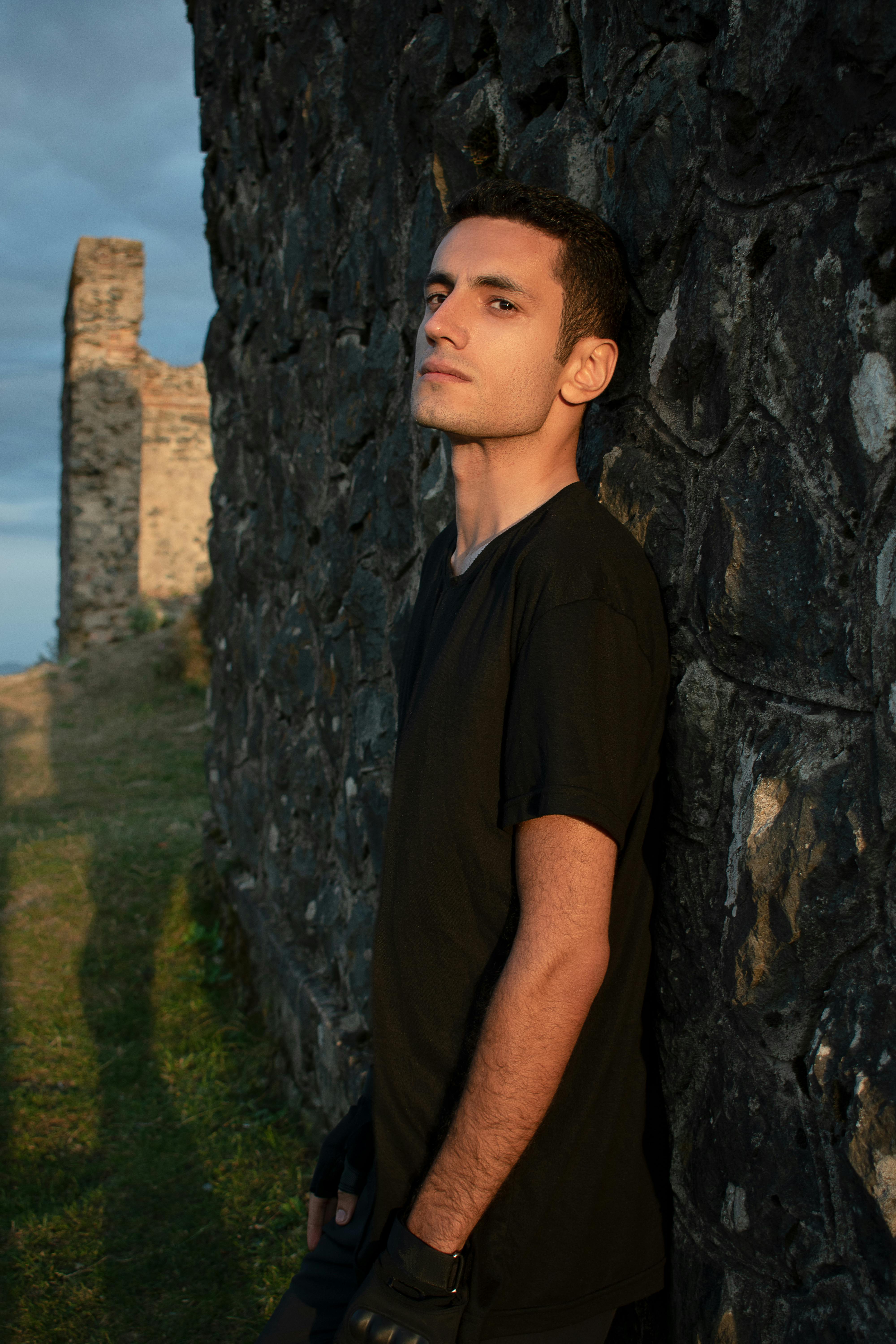 Man leaning against a stone wall at sunset with distant ruins.