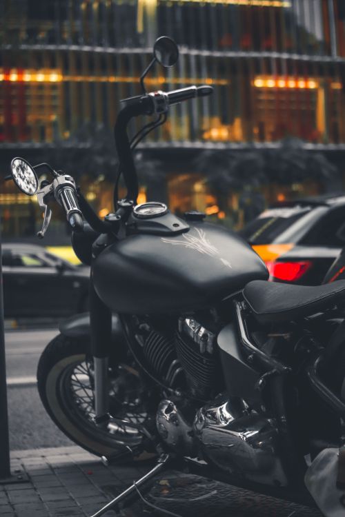 Free A sleek black motorcycle parked on a bustling city street with blurred traffic lights in the background. Stock Photo