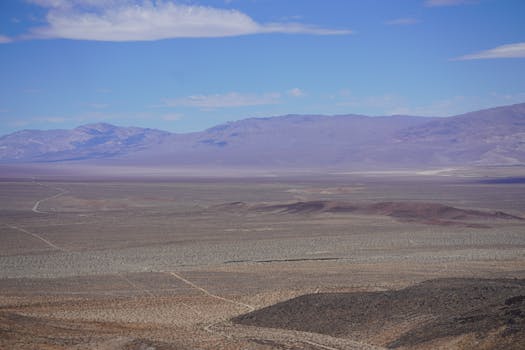 Wide-angle view of a desert landscape with distant mountains under a clear blue sky.