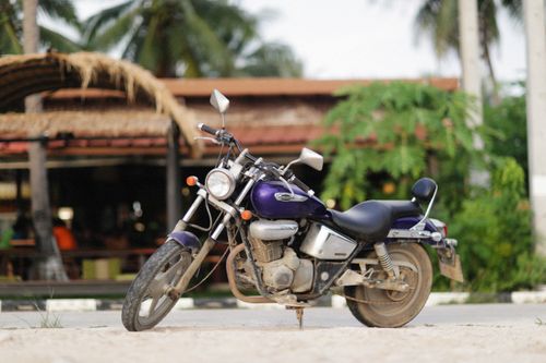 Free A purple motorcycle parked in front of a tropical outdoor cafe, under sunny skies. Stock Photo