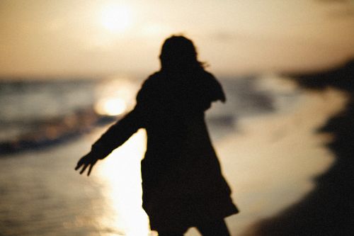 Free Silhouette of a person walking along the beach during a warm sunset. Stock Photo