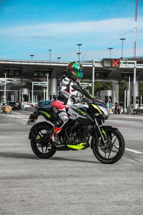 Free Motorcyclist on Bajaj Pulsar 200NS waits at an urban crossroad in vibrant gear. Stock Photo